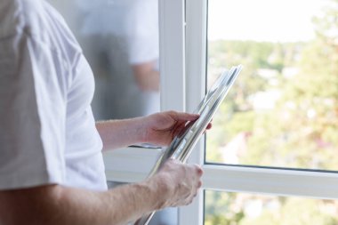 Pencerenin yanında duran ve elinde bir rulo renkli film tutan adam.