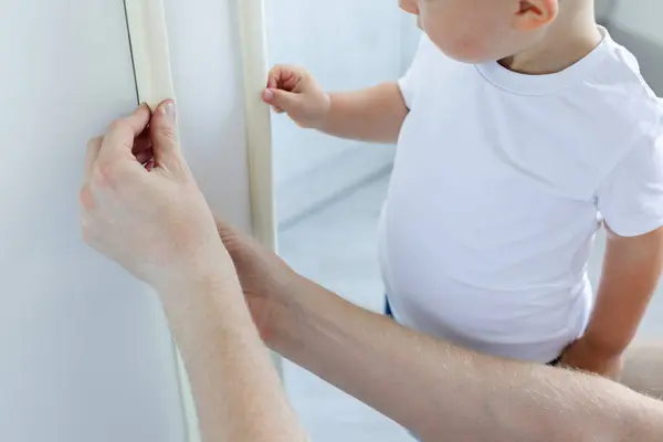 Küçük çocuk, babasının eve yumuşak köşe koruması kurmasına yardım ediyor. Küçük çocuklar için ev güvenliği. Seçici odak