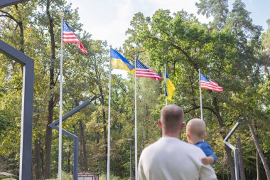 Ukrayna ve Amerikan bayraklarına karşı küçük bir çocuğu tutan adam. Arka görünüm