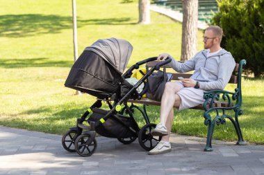 Babam parkta bebek arabasında uyuyan bir bebekle bankta oturuyor..