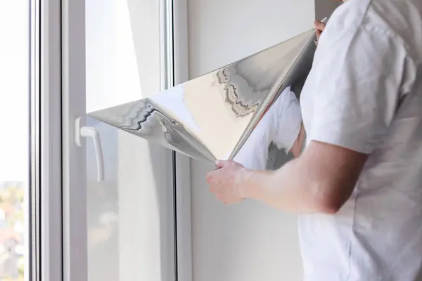 Evdeki camları güneş koruma filmiyle boyayan adam.