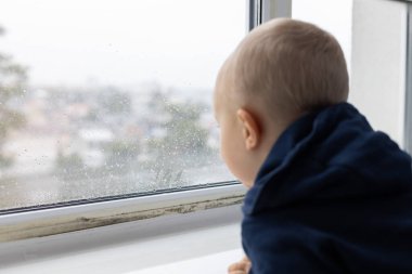 Su damlaları yoğunlaşmış ve siyah küf mantarı lekeleri olan küçük bir çocuk pencereden dışarı bakıyor. Seçici odak