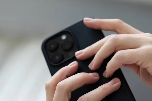 Kadın ellerinde siyah akıllı telefon. Düşük açı, yakın çekim.