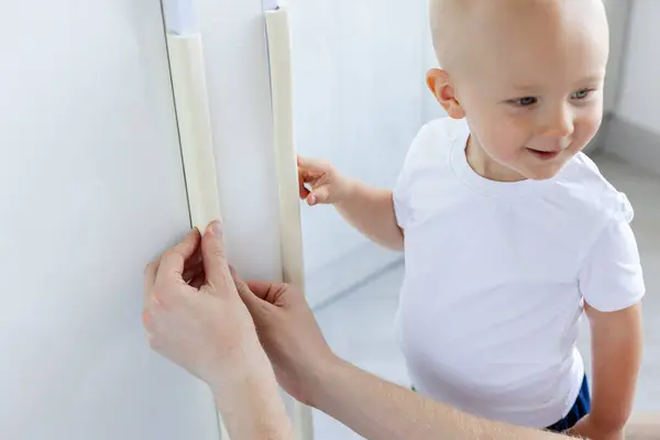 Küçük çocuk, babasının eve yumuşak köşe koruması kurmasına yardım ediyor. Küçük çocuklar için ev güvenliği. Seçici odak