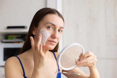 Gülümseyen kadın yüzüne krem maske takıyor. Sorunlu cilt için kozmetik