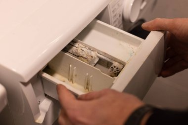 Küf, kir ve kireçlenme içeren çamaşır makinesi konteynırı açan adam. . 