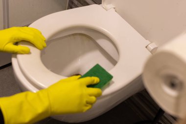 Kirli klozeti süngerle temizleyen sarı lastik eldivenli eller.. 