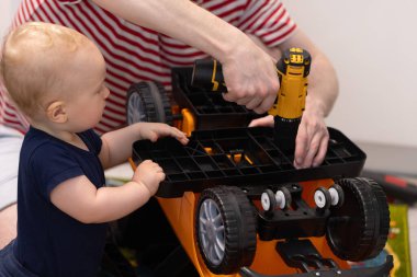 Küçük çocuk tuhaf bir şekilde babasının oyuncak bir arabayı tornavidayla tamir edişine bakıyor.