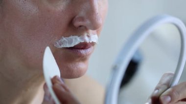 Aynanın önündeki kadın üst dudağından tüy dökücü krem çıkarıyor. - Yakın çekim. 4k görüntü