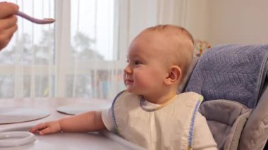 Bebek ilk önce kaşığa yemekle bakıyor ama sonra yemek istemiyor. 4k görüntü.