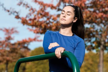 Bir fitness kadını Londra parkında sonbahar güneşinin tadını çıkarıyor. Elinde yeşil bir tırabzan var..