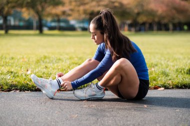 Spor bir kadın asfaltta oturmuş dantel ayakkabısını bağlıyor. Sonbaharda Londra Parkı 'nda..