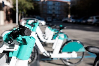 Kiralık e-bisikletler şehrin rıhtım istasyonunda arka arkaya park edilir. Sadece birincisi odaklanmış durumda. Güneşli bir gün. Ekoloji kavramı.