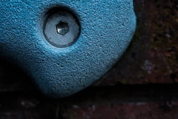 Close-up of artificial blue climbing hold on a brick wall. Texture and wall paper. Micro view of screw.
