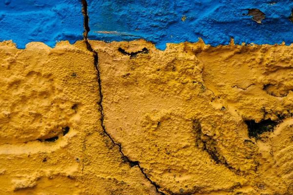 Wallpaper of a yellow and blue rough wall. A lot of cracks and holes.