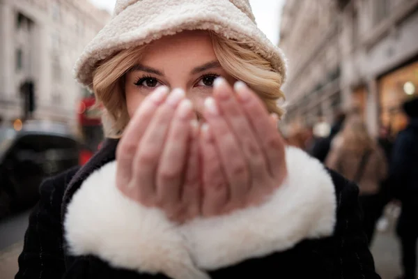 Head-shot of woman hiding her face in street. We can see her eyes and she in a busy street full with people. Winter vibes.