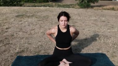 Young woman is sitting on a mat and stretching in a park. Yoga position. Relaxing and spirituality concept.