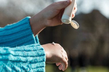 Unrecognizable person applying cream on hand with moisturize bottle. It is a sunny winter morning and she is in a park.