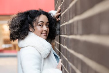 Curvy young woman posing on a brick wall. Her hands are on the wall and she is looking at camera.