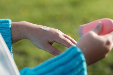 Close-up of woman hands applying moisturize on skin. She has a green grass background. Skin care concept.