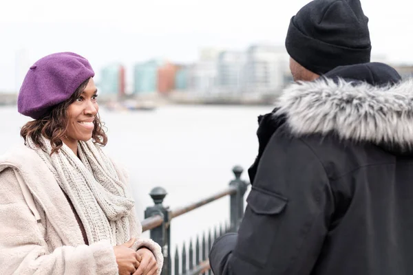Smiling deaf woman paying attention to her friend who is using sign language. River Thames and winter vibes.