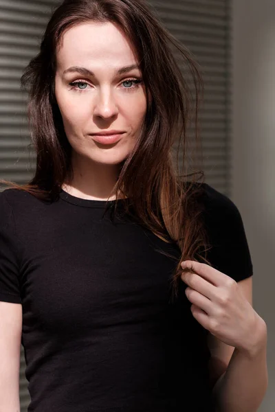Portrait of smiling caucasian woman looking at camera. She is wearing a black t-shirt and the sun is hitting on her face.