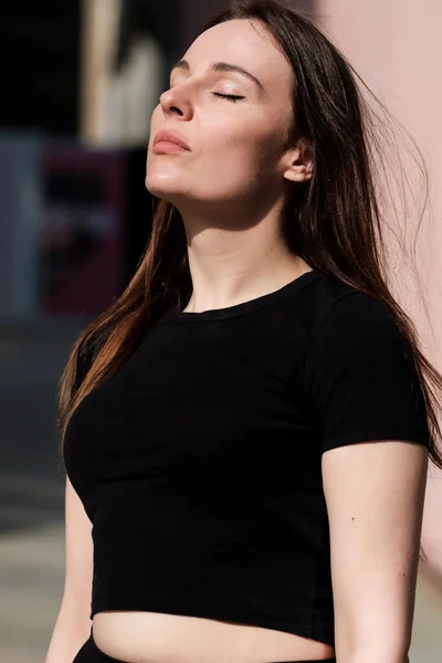 Relaxed portrait of caucasian woman with eyes closed outdoors. She is wearing a black top.