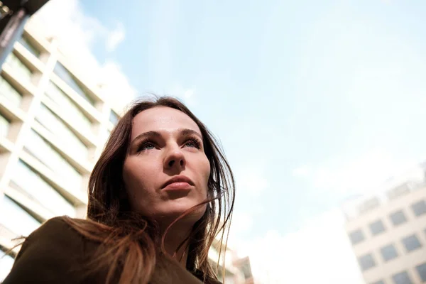 Close portrait of caucasian woman in an urban environment. Low point of view and she has a building behind.