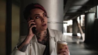 Modern çift cinsiyetli insan telefonla konuşuyor ve kahve içiyor. Bu bir mola ve o karanlık bir sokakta canlı konuşuyor..