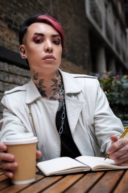 Masada elinde not defteriyle elinde kahveyle kameraya bakan Androgynous modeli. Yaratıcılık ve ilham konsepti artı ikili olmayan çeşitlilik yaşam tarzı konsepti.