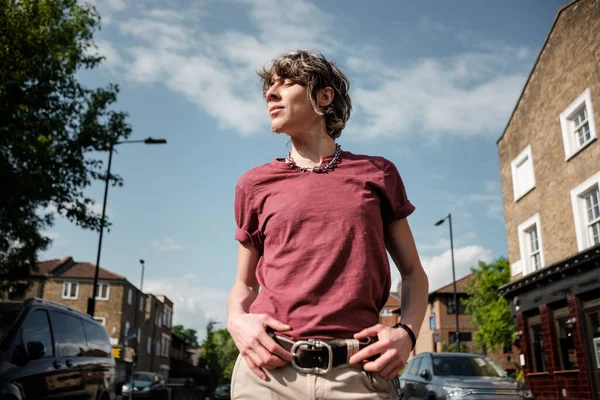 Androgynous person standing on the road enjoying the sunlight. There are many cars. Lgbtq, pride and diversity concept.