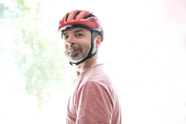カメラを見て赤でサイクリストのサイドビュー 彼は赤いヘルメットをかぶっていて 笑っている バックライトが点灯 スポーツのコンセプトで安全 — ストック写真