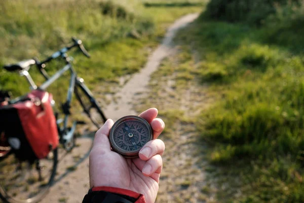 stock image Hand of unrecognizable cyclist holding compass. He is in the countryside, on a narrow path. There are grass everywhere. Adventure and healthy lifestyle concept.