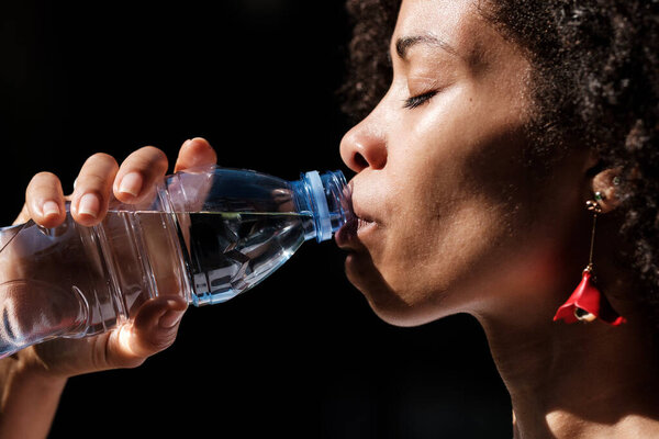 Close-up of black woman drinking water from a bottle. Healthy life style and alcohol-free drinks concept.