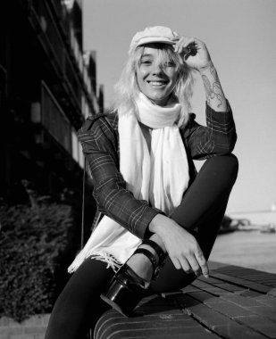 Smiling alternative female model is looking at camera sitting on stairs outside. Image made with medium format analog film camera. Monochrome. clipart