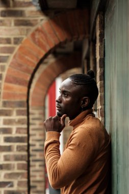 Düşünceli siyah erkek model yeşil kapıya yaslanıyor ve başka tarafa bakıyor. Yakışıklı model, refleksli ruh hali..