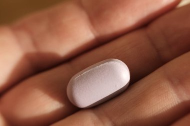 Tek bir pembe hapı açık elle tutarak, ilaç, sağlık, eczane kavramlarını, vitamin ve ilaçların tedavi ve sağlıktaki önemini,
