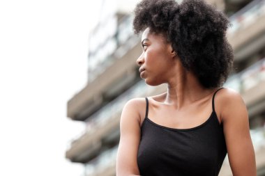 Diğer tarafa bakan kıvırcık modelin hassas portresi. Arkasında bulanık bir bina var ve büyük bir şehirden gelen stresi hissedebiliyoruz..