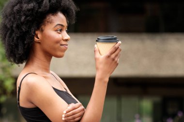 Dinlenmiş ve gülümseyen kıvırcık kadın molasında elinde bir fincan kahve tutuyor. Rahatla ve boş zaman kavramı.