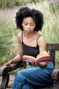 Parkta kitap okuyan genç bir kadın. Bankta oturuyor ve çok huzurlu ve rahat görünüyor. İlham ve edebiyat kavramı.