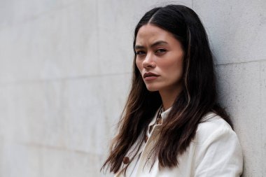 Kameraya bakan sert kadının portresi. Melez ırk, açık havada beyaz bir duvara yaslanıyor. Güven ve tutum konsepti.