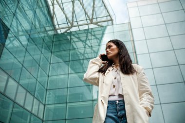 Kozmopolit bir ortamda telefonla konuşan melez bir kadının portresi. Arkasında cam bir bina var. İletişim ve yalnızlık kavramı.