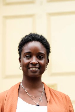 Bulanık sarı kapının önündeki siyah kıvırcık kadının kafasından vurulmuş. Doğruca kameraya bakıyor ve küpeler ve tasmalar takıyor..