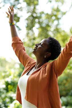 Siyahi kadın silahlanmış, barışçıl ve ruhani bir jest yapıyor. Doğada ve arka planda bulanık ağaçlar var. Onun gözleri kapalı. İnanç ve başarı kavramları.
