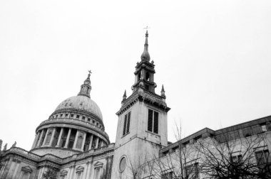 Londra 'daki Aziz Paul Katedrali' nin koyu siyah ve beyaz analog fotoğrafları. Açık gökyüzüne karşı kubbe ve çan kulesi sergileniyor. Ağaç dalları biraz kış atmosferi katıyor.