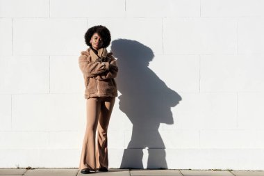 Beyaz duvarın önünde duran ve dışarıdaki kameraya bakan genç siyah bir model. Güneşli kış günü. O kalın bir ceket ve eşarp giyiyor. Kıvırcık saçlı.