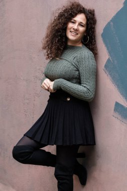 Dışarıdaki pembe duvara yaslanmış olgun bir model. Soğuk kış gününde siyah etek ve kazak giyiyor..