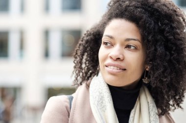 Çekici, kıvırcık, siyah bir kadının açık havaya bakışları. Kış mevsimindeyiz ve o ceket ve atkı giyiyor..