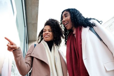 Dışarıdaki dükkanın penceresine heyecanlı bir şekilde bakan birkaç zenci bayan arkadaş. Bir tanesi içine bir şey doğrultuyor ve mutlu görünüyorlar. Kış soğuk günü.