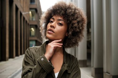 Londra 'da dar bir sokakta poz veren gevşek kıvırcık kadın model. Yeşil bir ceket giyiyor ve yavaşça sağ eliyle dokunuyor..